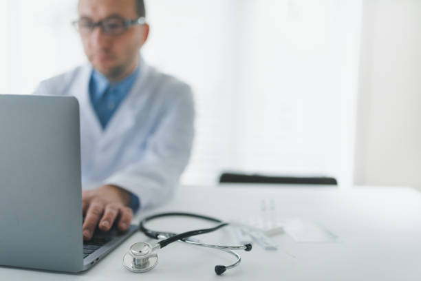 Doctor in his office working on laptop. He is discussing with his patients using video conference software