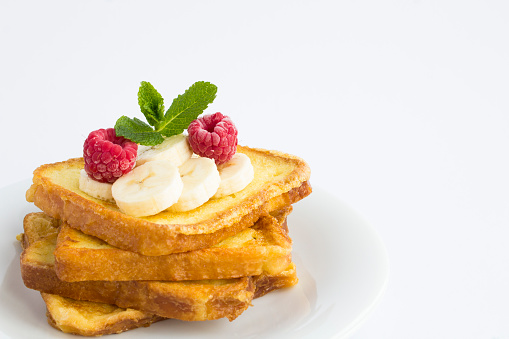 Close-up on french toasts with banana and raspberry on the white plate on the white background. Copy space.