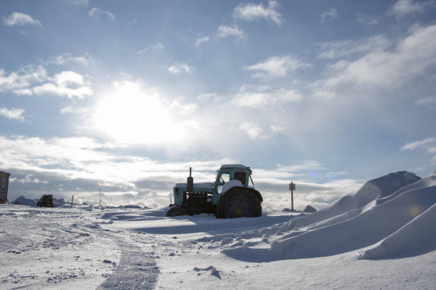 Tractor on a deserted snow-covered field against a cloudy sky.
