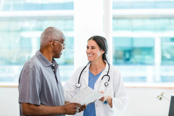 Female surgeon smiles at senior patient holding brochure The mid adult female specialist smiles at her senior adult male patient as he asks a question about the information in the brochure. orthopedist stock pictures, royalty-free photos & images