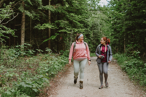 Two Caucasian women in sports clothes walking in nature and taking photos for their blog.