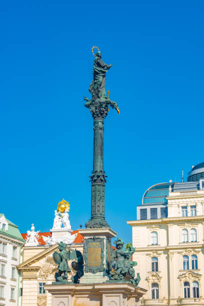 Marian Column monument with Virgin Mary at top and four cherubs battling adversary creatures representing heresy, hunger, plague, war located at Am Hof square, historical downtown in Vienna, Austria monumento a la columna mariana con la virgen maría en la parte superior y cuatro querubines luchando contra criaturas adversarias que representan herejía, hambre, peste, guerra ubicadas en la plaza am hof, centro histórico de viena, austria.