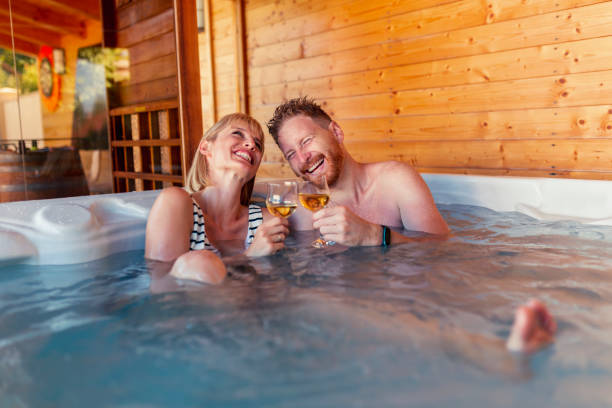 Couple drinking wine and relaxing in hot tub Beautiful young couple in love relaxing, making a toast  and drinking wine in a hotel resort spa center hot tub, having fun while on a vacation hot tub stock pictures, royalty-free photos & images