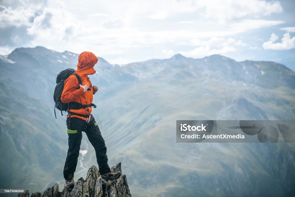 Mountaineer scrambles up summit of pinnacle Stormy day with lofty clouds Mountain Peak Stock Photo