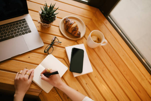 istock Young woman freelancer working online using her laptop, sitting in a coffee house and drinking coffee. Top view. 1367406941