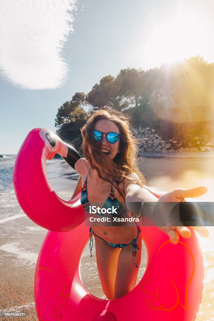 Smiling young woman with inflatable flamingo at the beach Happy young woman with inflatable flamingo at the beach Summer Stock Photo
