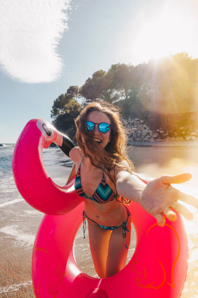 Smiling young woman with inflatable flamingo at the beach stock photo