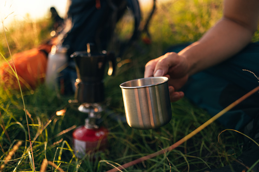 Close up shot of anonymous man holding a cup of coffee while camping in nature.
