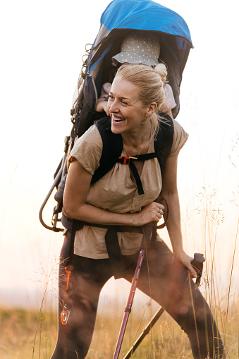 Beautiful blonde woman on a walk carrying her child in a backpack baby carrier. She is laughing on looking away.