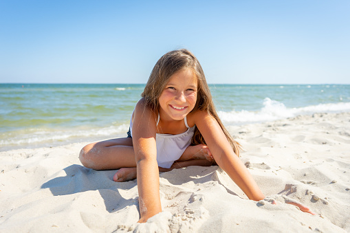 Cute little girl is sitting on the sand by the sea. Vacation on summer