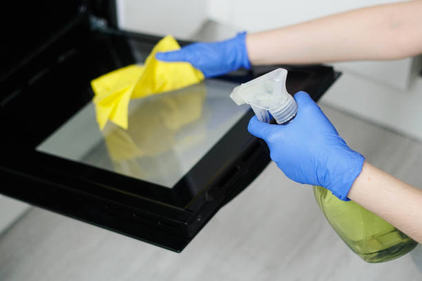 Closeup on woman's hands in protective rubber gloves cleaning oven with rag. Housewife splashes detergent onto the dirty surface of the kitchen oven. Closeup on woman's hands in protective rubber gloves cleaning oven with rag. Housewife splashes detergent onto the dirty surface of the kitchen oven. cleaning stove domestic kitchen human hand stock pictures, royalty-free photos & images