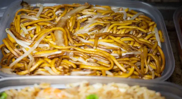 Close and selective focus on a plastic tub of plain chow mein or noodle, onion and beansprouts bought from a Chinese takeout with intentional shallow depth of field and bokeh