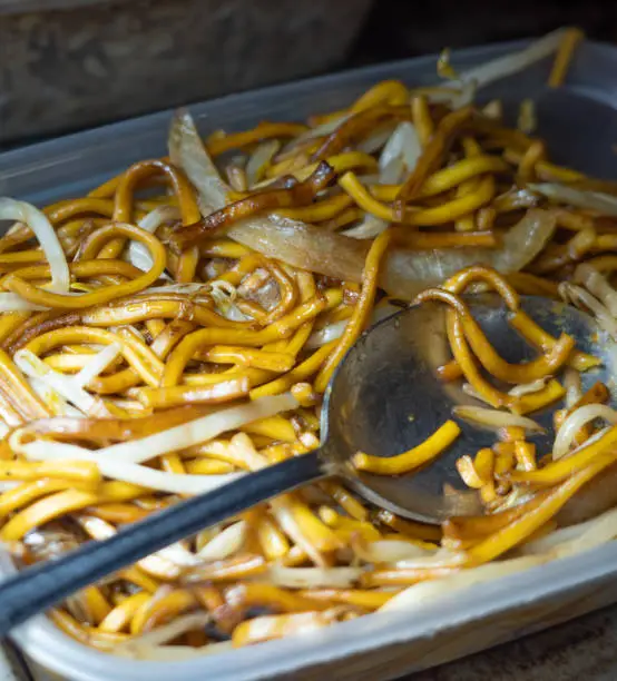Close and selective focus on a plastic tub of plain chow mein or noodle, onion and beansprouts bought from a Chinese takeout with intentional shallow depth of field and bokeh