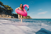 Happy young woman with inflatable flamingo enjoying the sunny day at the beach