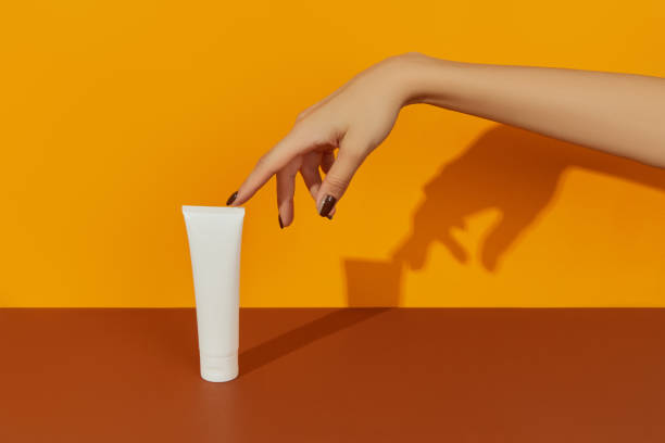 istock Womans hand holding cosmetic on orange background with copy space 1367413862