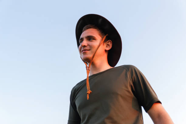 joven sonriendo con sombrero de vaquero contra el cielo azul. macho sobre fondo de cielo azul, al aire libre en prado. concepto de agricultura.  wow y divertido. primer plano. - cowboy blue meadow horizontal fotografías e imágenes de stock