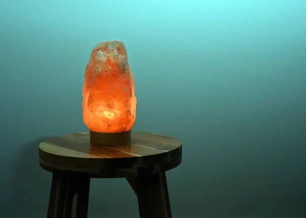 Photo of Himalayan salt lamp glowing on wooden table near turquoise wall at night