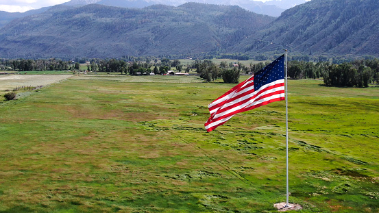 American Flag Flying in a meadow nestled in the rocky mountains in southwestern Colorado near Telluride and Ouray on a bright partly cloudy day with beautiful clouds