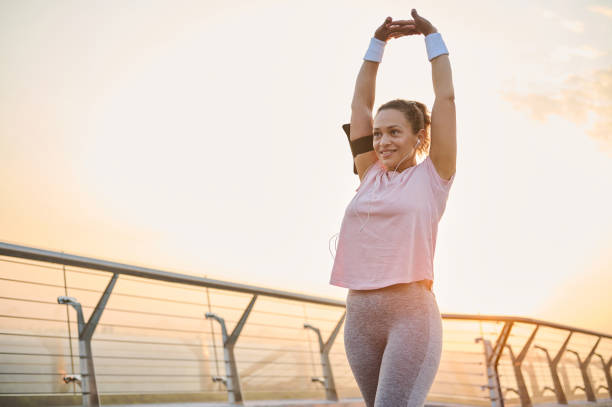 Happy determined female athlete, sportswoman enjoys morning cardio workout, stretches her arms, raising them up, exercises at sunrise. Fitness, health, body care, sport and active lifestyle concept feliz atleta femenina segura, deportista disfrutando del entrenamiento cardiovascular matutino, estirando los brazos, levantándolos, haciendo ejercicio al amanecer. concepto de fitness, salud, cuidado corporal, deporte y estilo de vida activo