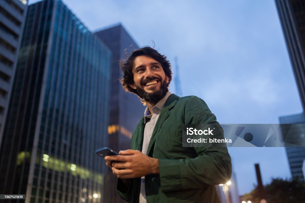 View of young man using a smartphone at night time with city view landscape in the background. High quality photo View of young man using a smartphone at night time with city view landscape in the background. Mobile phone, technology, urban concept. High quality photo Men Stock Photo
