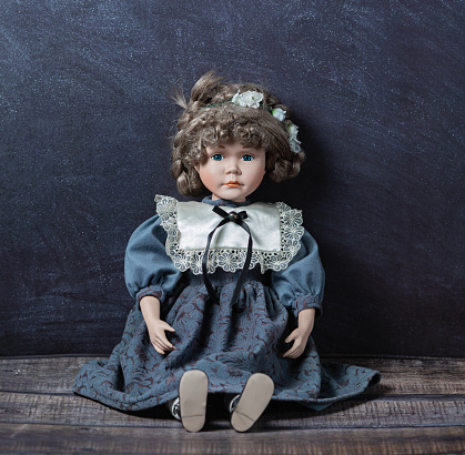 Amazing realistic vintage toy with blue eyes.The doll dressed in a gray-blue dress with lace and has a blond hair. Selective focus. Porcelain doll.