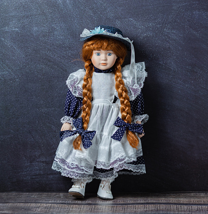Amazing realistic vintage toy with blue eyes.The doll dressed in a white-blue dress with lace and has a red hair. Selective focus. Porcelain doll.