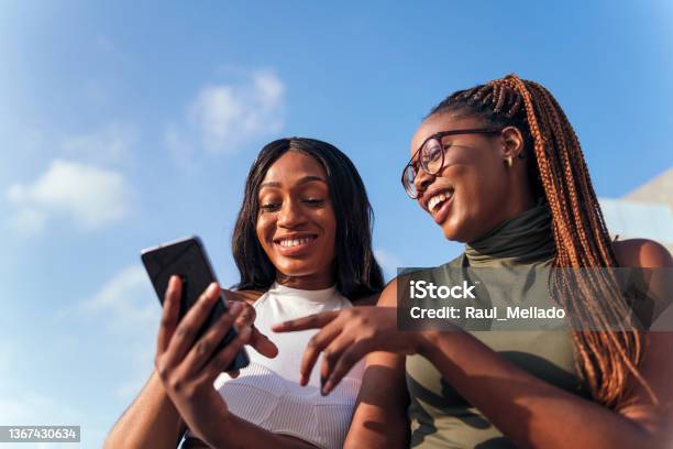 Two Young African Women Having Fun Looking Phone Stock Photo - Download Image Now - Friendship, Telephone, African Ethnicity