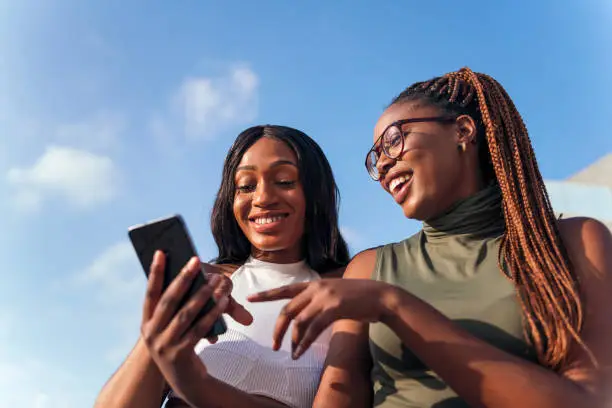 Photo of two young african women having fun looking phone