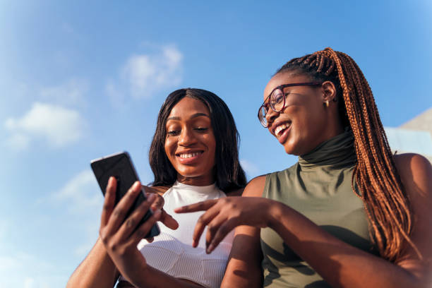 two young african women having fun looking phone - girl woman imagens e fotografias de stock