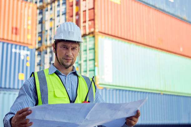 istock Engineer stand holding schematic paper or blueprints in a container yard. 1367434191