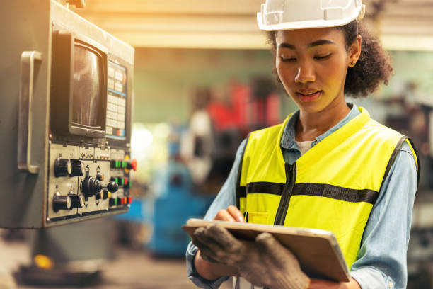 istock Standing in front of a control panel, a female industrial electrical engineer with a safety hardhat on her head and a tablet in her hand checks and maintains CNC machines in a factory. 1367450816