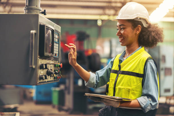 vor einem bedienfeld stehend, überprüft und wartet eine wirtschaftselektrikerin mit sicherheitshelm auf dem kopf und einem tablet in der hand cnc-maschinen in einer fabrik. - electricity control panel control order stock-fotos und bilder