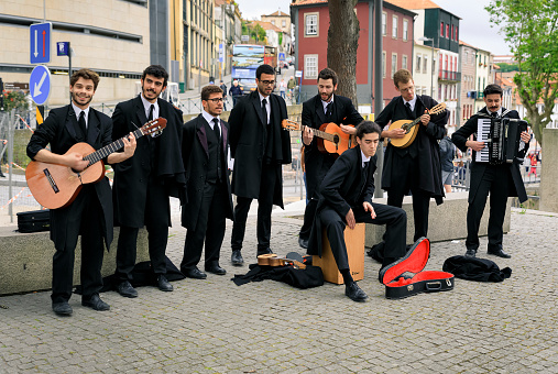 Porto, Portugal - May 31, 2018: A band of young male students in black capes on the Douro river bank playing instruments and singing for money