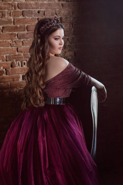 красивая молодая симпатичная женщина-принцесса в длинном фиолетовом платье королевы и короне, с длинными волосами и макияжем в помещении в - women crown princess 20s стоковые фото и изображения