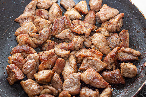 Pork meat is fried in a pan. Drops of oil in a frying pan. Close up.