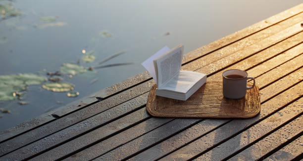 cup of coffee and book on wooden pier on summer lake stock photo
