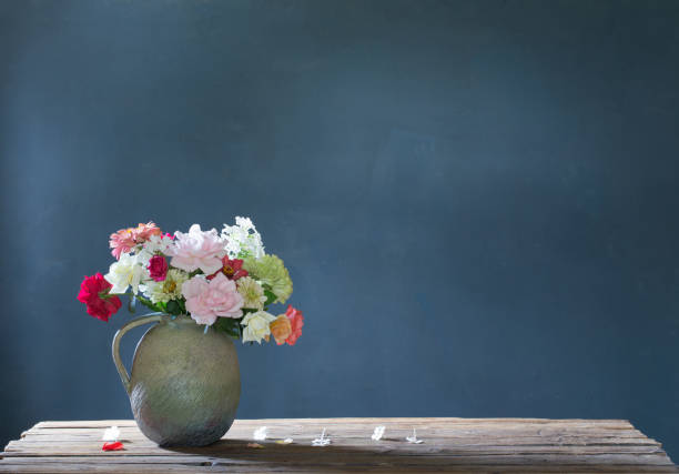 summer flowers in ceramic jug on wooden table on blue background