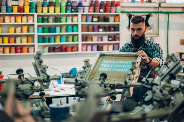 männlicher arbeiter mit druckmaschine in einer werkstatt - silk screen fotos stock-fotos und bilder