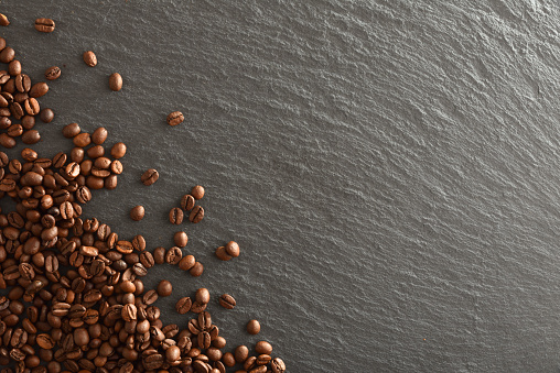 Dark background with heap of selected natural coffee beans in one corner on slate base. Top view. Horizontal composition.