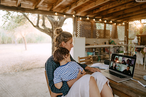 Photo of a female freelancer working from a remote location with a child in her lap. They are on video call.