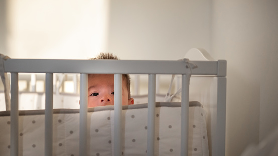 Baby escapes from the crib by climbing over the bars. The child climbs over the bed rail. Kid aged about two years (one year nine months)