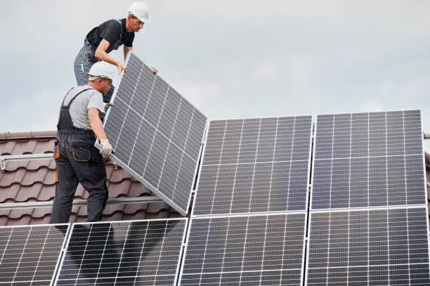 Photo of Man worker mounting solar panels on roof of house.