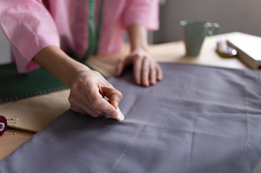 High angle close up view of an unrecognizable successful Caucasian female fashion designer working in her loft fashion studio, designing her clothes and using chalk to draw on it