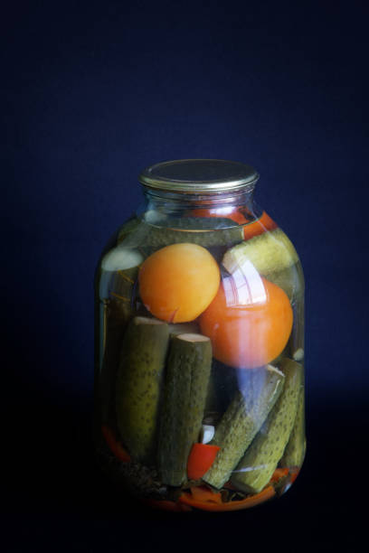 Tinned cucumbers and tomatoes in a large three-liter jar on a dark blue background. Farm harvest and homemade products concept. Close-up