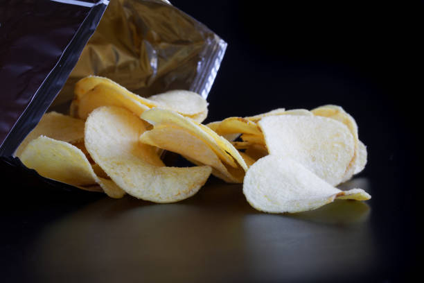 istock Potato chips sprinkled from a foil-lined packaging bag on a dark surface 1367499041