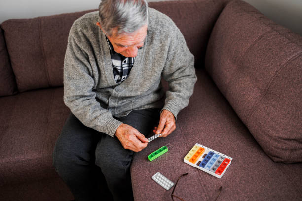 un anciano jubilado vierte píldoras de un frasco de píldoras en su mano mientras organiza el medicamento en un organizador semanal de píldoras. - real people one person multi colored part of fotografías e imágenes de stock