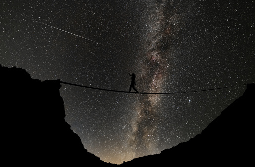 Tightrope walker silhouette in between rocks in the starry night. Mikly way galaxy on the sky.