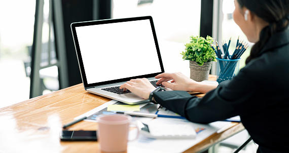 Vista lateral de la mujer usando una computadora portátil en la oficina en casa con una toma recortada. Portátil de pantalla en blanco para la visualización del producto. photo