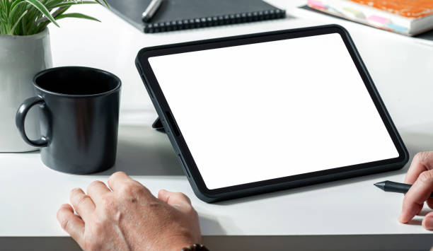istock Digital portable tablet computer white screen mockup. Man working on digital tablet at his desk. 1367508595