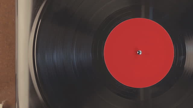 Detail of a woman's hand putting vinyl record into the player. Footage has a retro look. Top view of record spinning towards the end.